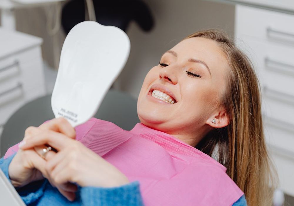 Dental patient reclining in the chair, smiling as she checks her teeth in a hand mirror